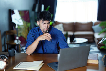 Portrait of an Asian man using a computer and note book to record his work