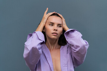 Pretty stylish woman in purple shirt posing on blue wall background, long dark beautiful hair, natural makeup, soft skin