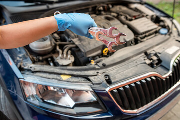 Close-up of car mechanic's hand holding wrench to remove part in engine compartment of car.