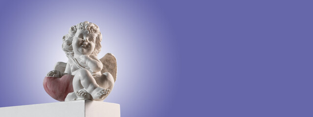 Figurine of an angel Cupid on the podium with a red heart on a very peri purple background . Valentine's Day.