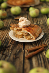 A piece of homemade apple pie with a ball of ice cream on a plate and the ingredients for it - fresh apples, brown sugar and cinnamon spices. 