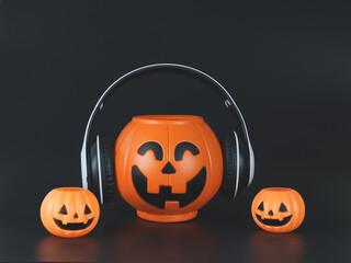 big plastic halloween pumpkin  coverd with headphones, isolated on black  background with smaller pumpkins,  copy space. Halloween music or podcast.