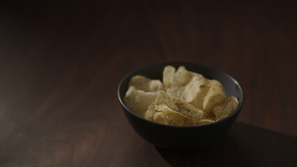 organic potato chips with black pepper in black bowl on walnut table