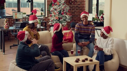 Diverse people exchanging presents at christmas party in office, celebrating holiday season together with xmas ornaments and lights. Making surprise gifts as seasonal winter tradition. - Powered by Adobe