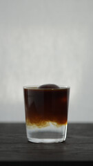 Vertical shot of making espresso tonic in tumbler glass, espresso over ice ball