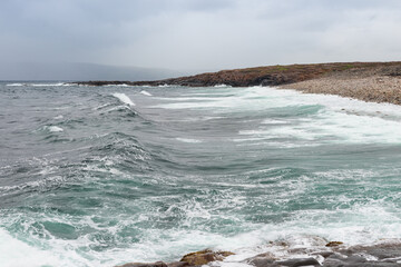 Dangerous sea wave crashes on a rocky coastline with splashes and foam before a storm in the Barents Sea