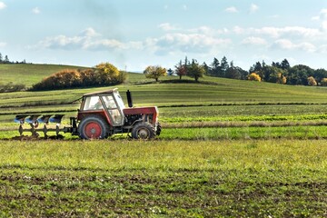 Fototapeta premium Old red Tractor Plowing in Autumn, Farmer plowing stubble field in tractor preparing plows the land. Agricultural works at farmlands in Czech Republic.
