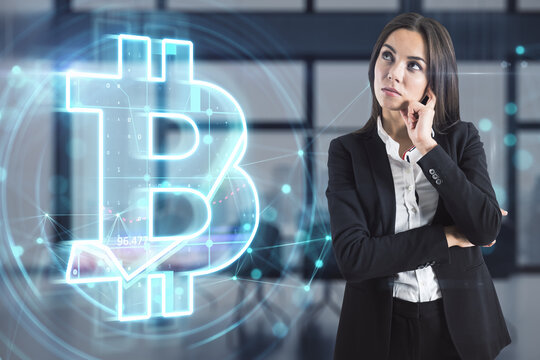 Attractive young european businesswoman with glowing bitcoin hologram on blurry office interior background. Metaverse, cryptocurrency and crypto concept. Double exposure.