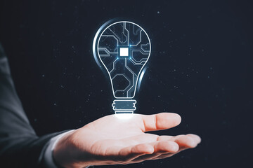 Close up of businessman hand holding abstract glowing light bulb with chip hologram on blurry dark...