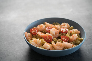 Fusilli with shrimps, cherry tomatoes and pesto in a blue bowl on concrete background