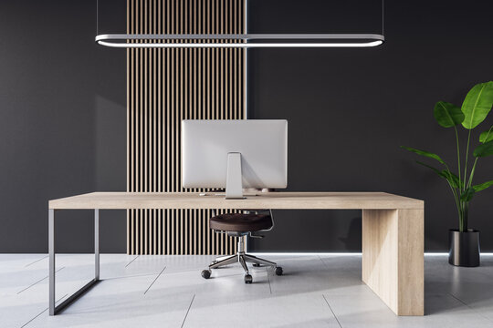 Front view on modern computer on stylish light wooden work table in spacious cabinet with dark wall background and ceramic tiles floor. 3D rendering
