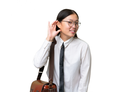 Young Asian business woman over isolated background listening to something by putting hand on the ear