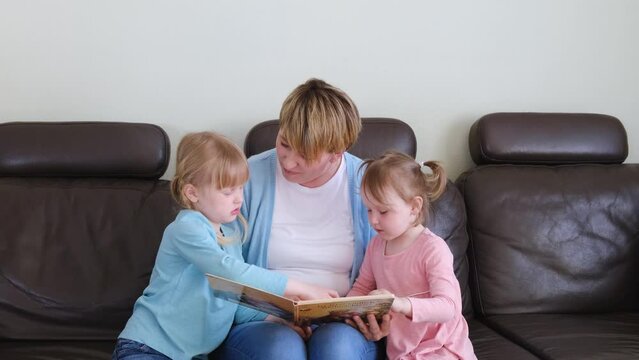 Mother and preschool cute daughters having fun at home, eading fascinating fairy tale book.
