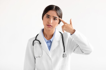 Tired sad millennial indian woman doctor in coat show hand gesture, pistol near temple