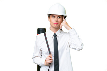Young architect woman with helmet and holding blueprints over isolated background having doubts and thinking