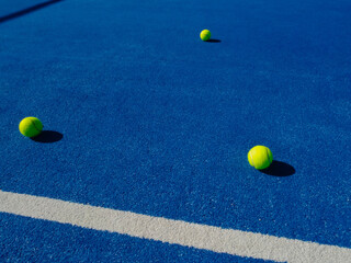 THREE BALLS ON A BLUE PADDLE TENNIS COURT SURFACE