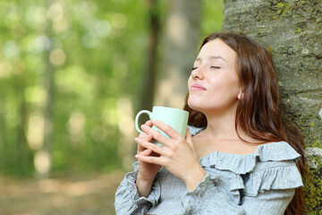 Woman relaxing drinking coffee sitting in a forest