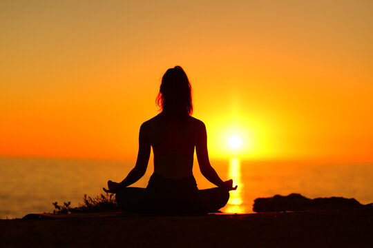 Silhouette of a woman doing yoga with sunset sun