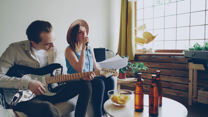 Creative musical duet is practising at home attractive woman is singing in microphone and handsome man is playing the guitar. Young cheerful people are wearing casual clothes.