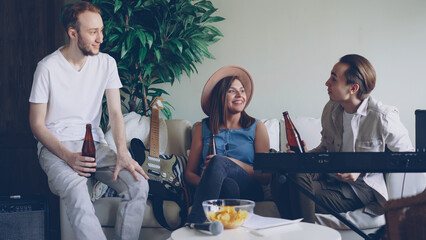 Musical group bearded guys and attractive blond girl are celebrating new song talking, laughing and drinking beer. Successful people concept.