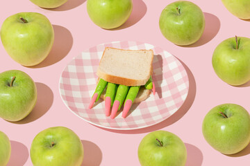 Halloween creative layout with witch hand figurine in sandwich on a plate and green apples around...