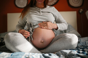 Belly of pregnant woman and soft toy close-up in real bedroom interior.
