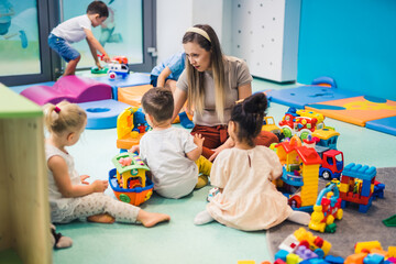 preschoolers sitting on the floor surrounded plenty of toys and enjoying with their teacher, nursery. High quality photo