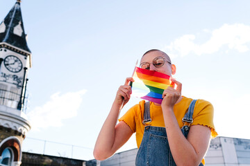 Young transgender person covering face with rainbow flag