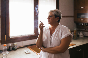 Depressed woman smoking cigarette in kitchen at home