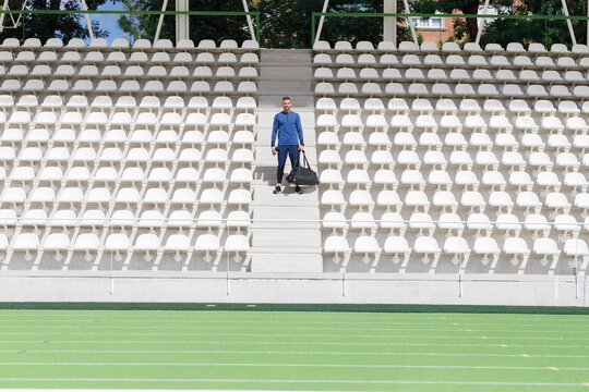 Athlete with bag standing amidst seats in stadium