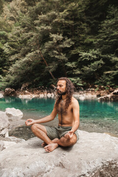Shirtless young man meditating on rock