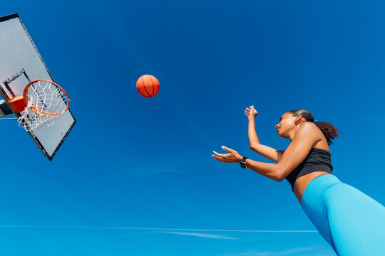 Sportswoman throwing basketball in hoop on sunny day