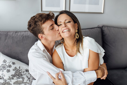 Teenage boy kissing mother on cheek at home