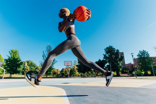 Young sportswoman with basketball jumping in sports court