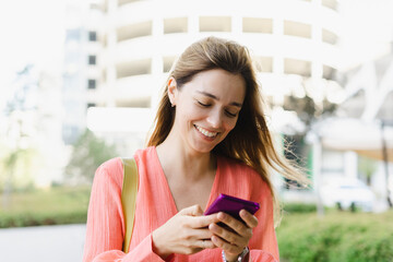 Happy woman using smart phone in front of building