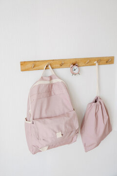 Pink color backpacks and alarm clock hanging on wall hook