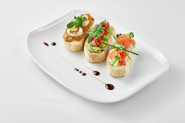 Set of bruschetta with salmon, avocado and goat cheese in a white plate on a white background. Close-up, selective focus.