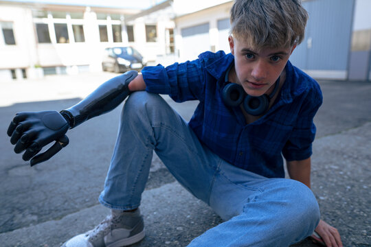 Boy with amputated arm sitting on footpath