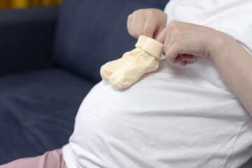 Little socks for future child. Yellow baby socks on the belly of pregnant woman. Clouse up