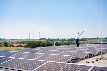 Mature businessman with arms raised amidst solar panels on rooftop