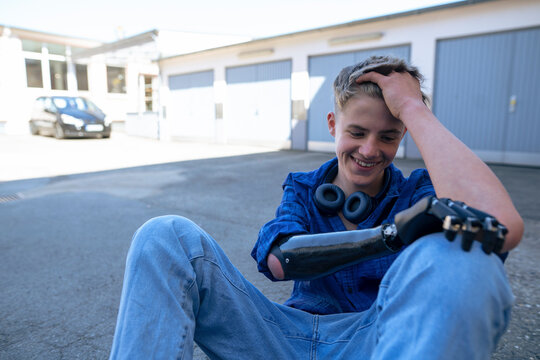 Happy teenage boy looking at amputated arm sitting with head in hand