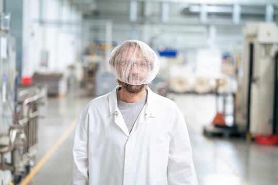 Man wearing lab coat and disposable cap standing in industry