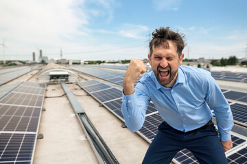Businessman with mouth open gesturing fist in front of solar panels