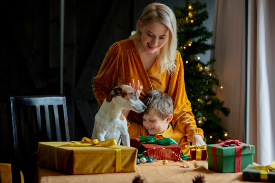 Mother and son with dog standing by wrapped gifts on table at home