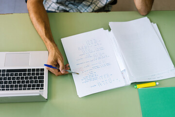 Teacher checking math paper by laptop in classroom