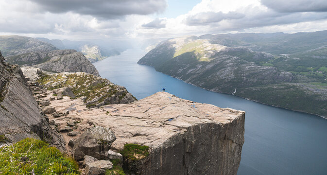 Famous Pulpit rock by Lysefjorden fjord with hiker standing at edge, Norway