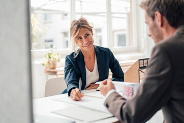 Businesswoman discussing with client reading agreement at office