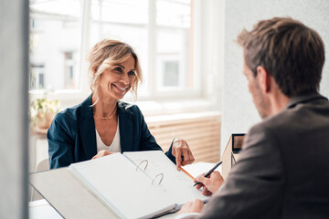 Smiling real estate agent assisting customer signing agreement at office