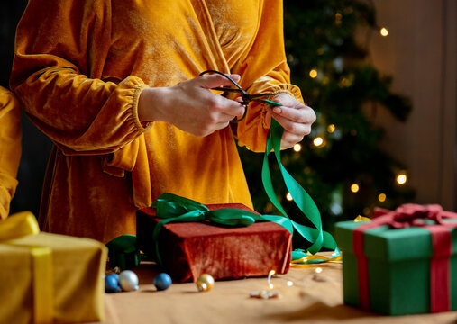 Woman Cutting Ribbon Over Christmas Gift At Home