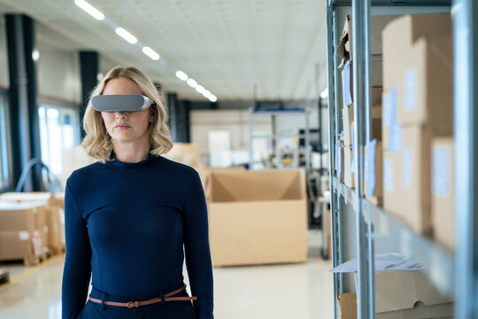 Blond businesswoman wearing virtual reality simulator standing by rack
